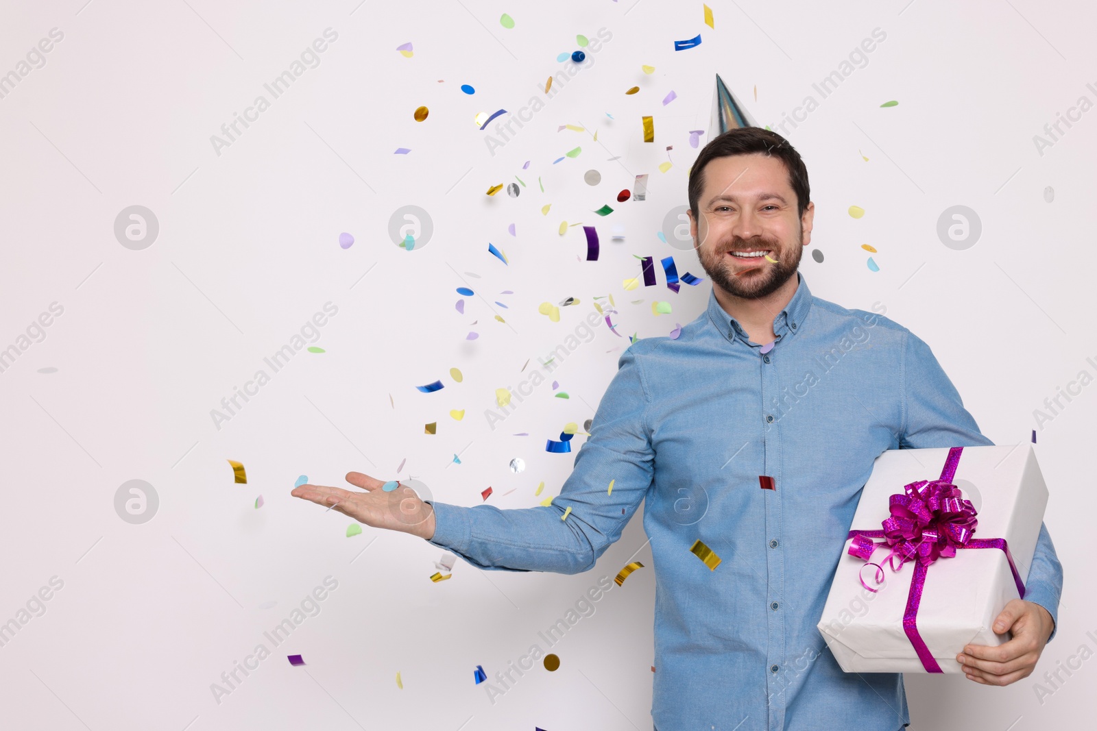 Photo of Happy man with gift box under falling confetti on white background, space for text. Surprise party