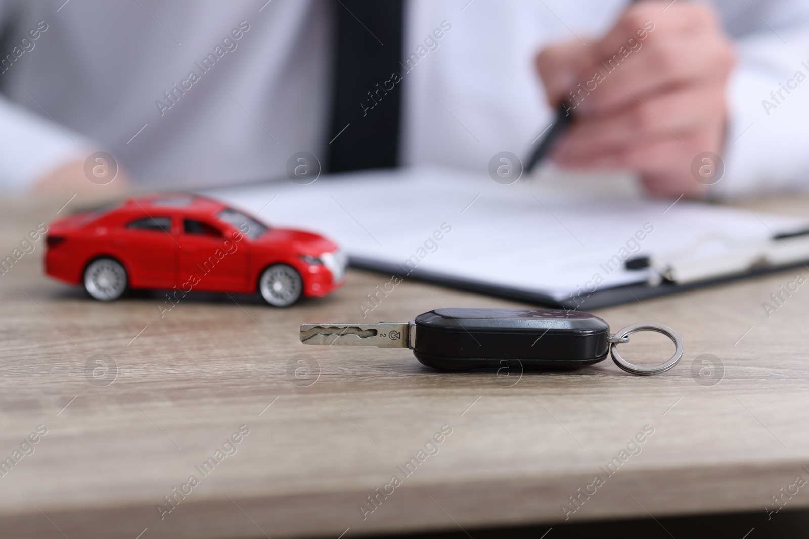 Photo of Man signing car purchase agreement at wooden table, focus on key. Buying auto