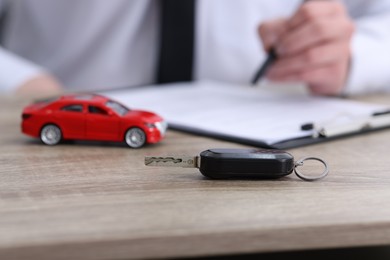 Photo of Man signing car purchase agreement at wooden table, focus on key. Buying auto