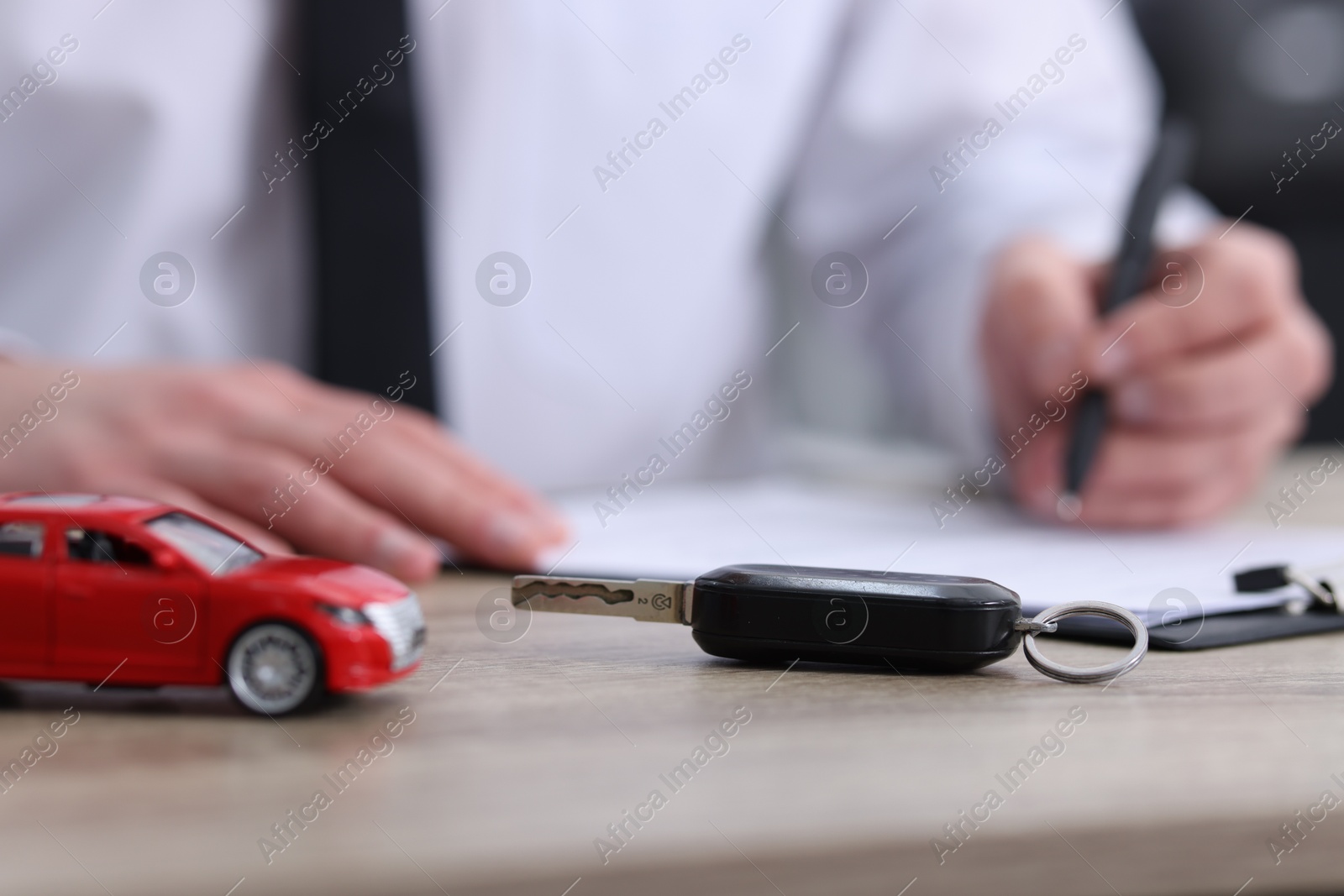 Photo of Man signing car purchase agreement at wooden table, focus on key. Buying auto