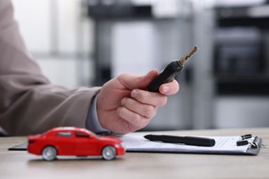 Photo of Man with car key at table indoors, selective focus. Buying auto