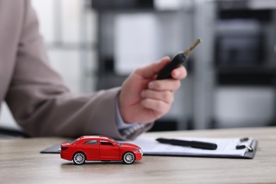 Photo of Man with key at table indoors, focus on car model. Buying auto