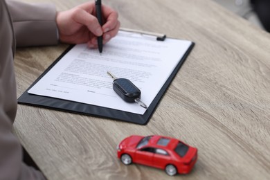 Photo of Man signing car purchase agreement at wooden table, selective focus. Buying auto