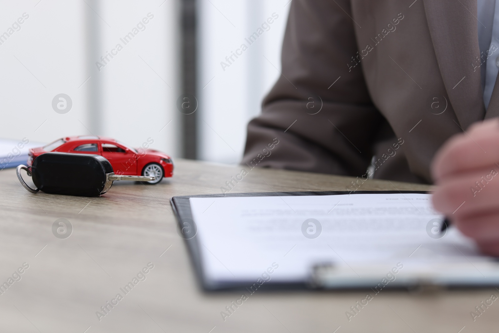 Photo of Man signing purchase agreement at wooden table indoors, focus on key and car model. Buying auto