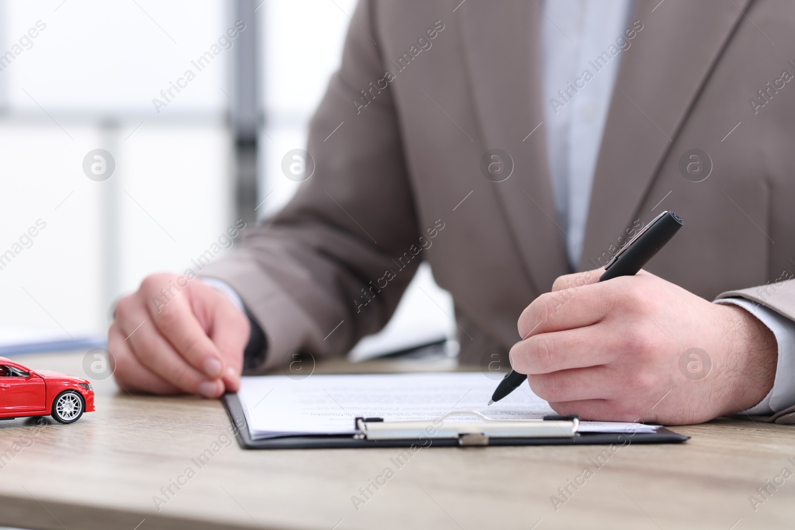 Photo of Man signing car purchase agreement at table indoors, selective focus. Buying auto