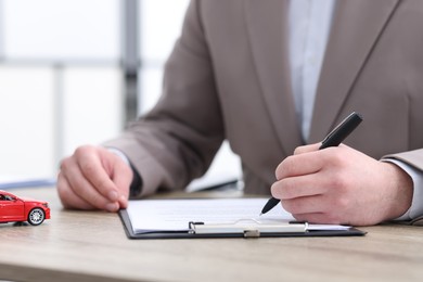 Photo of Man signing car purchase agreement at table indoors, selective focus. Buying auto