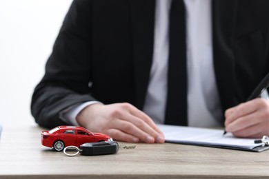 Photo of Man signing purchase agreement at wooden table, focus on car model and key. Buying auto