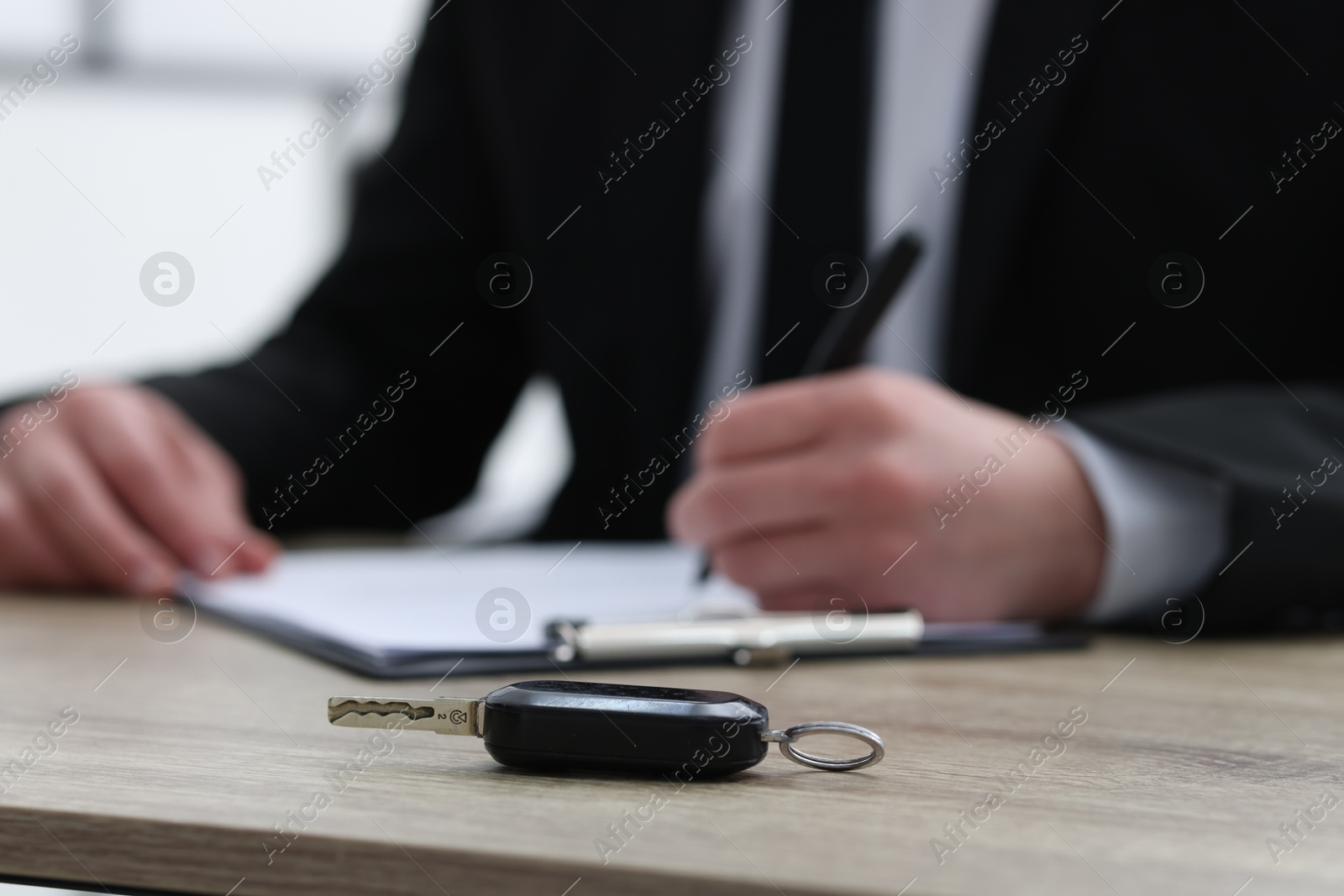 Photo of Man signing car purchase agreement at wooden table, focus on key. Buying auto