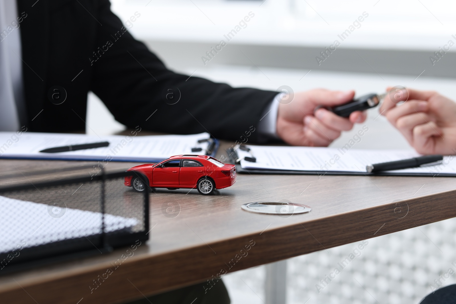 Photo of Salesman giving key to buyer at wooden table in office, focus on car model. Buying auto