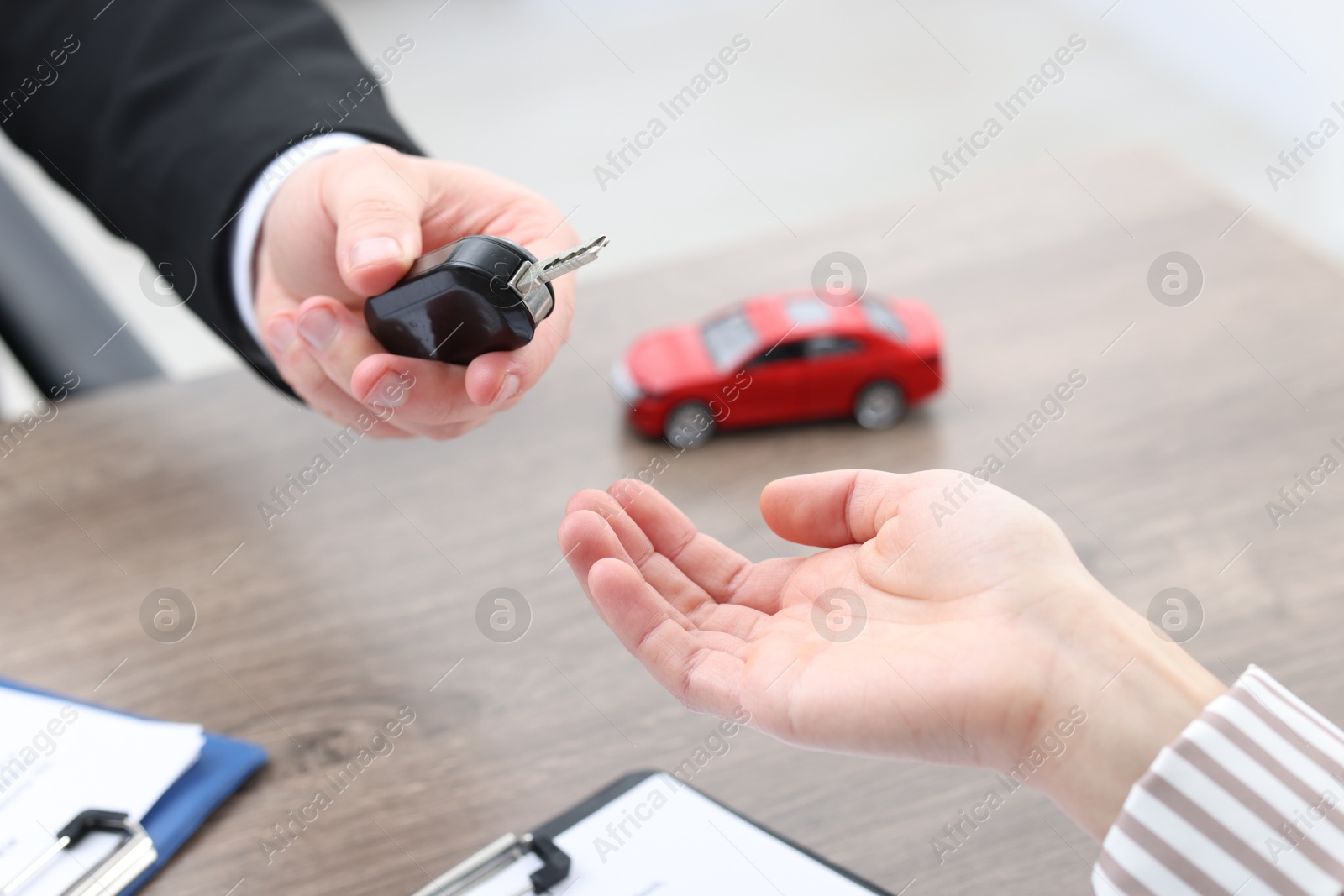 Photo of Salesman giving key to client at wooden table in office, closeup. Buying auto