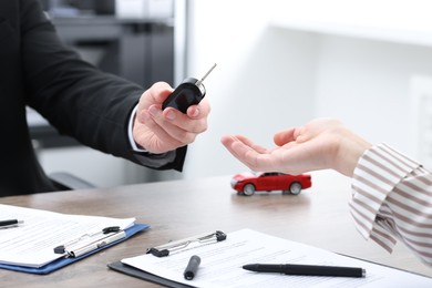 Photo of Salesman giving key to client at wooden table in office, closeup. Buying auto