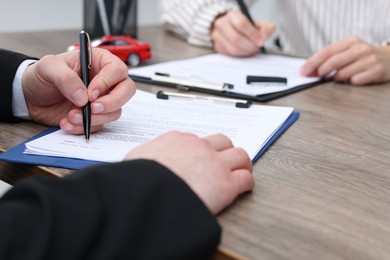 Photo of Salesman and client signing documents at wooden table, selective focus. Buying auto