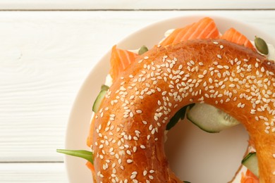 Photo of Delicious bagel with salmon, cream cheese and cucumber on white wooden table, top view. Space for text