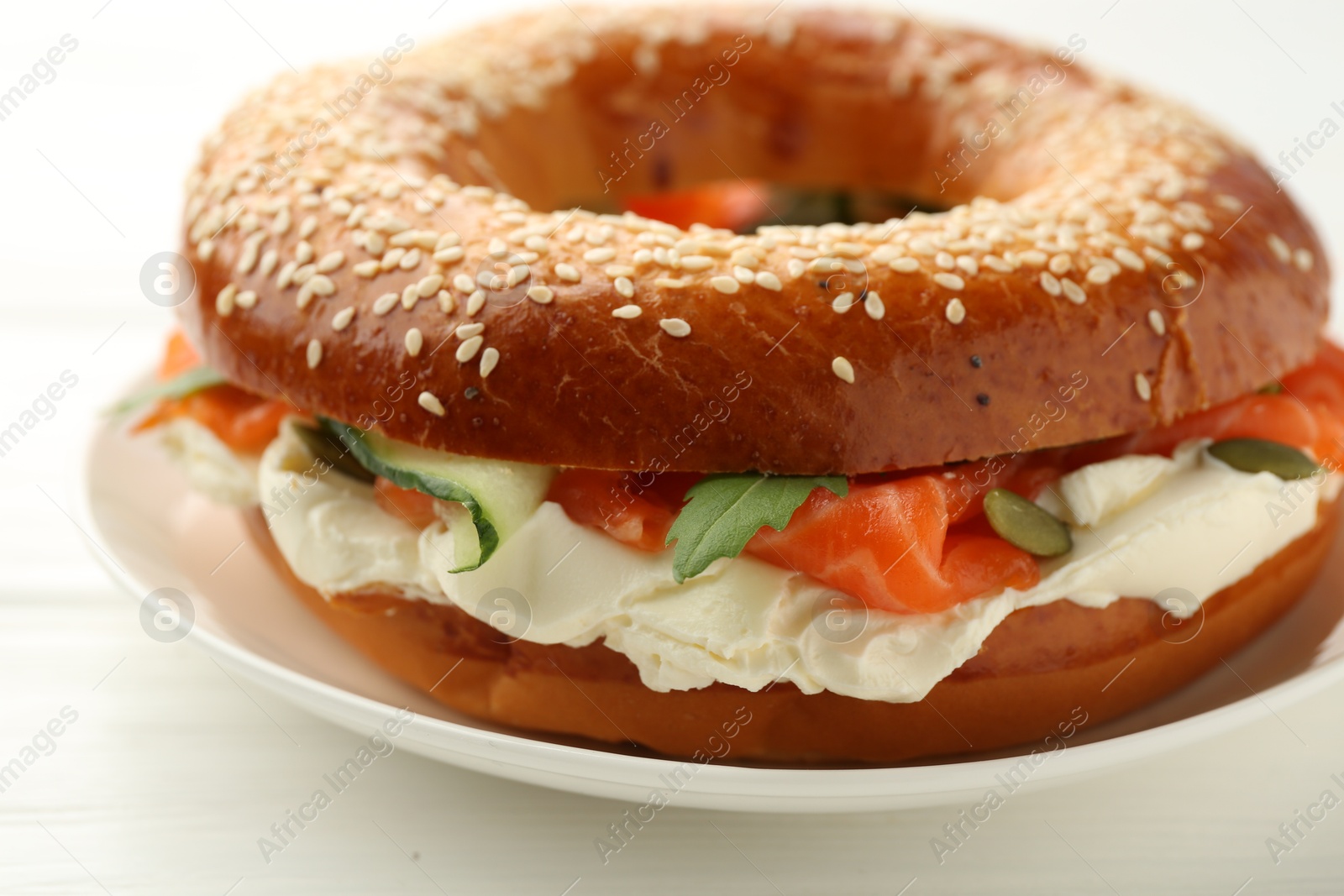 Photo of Delicious bagel with salmon and cream cheese on white wooden table, closeup