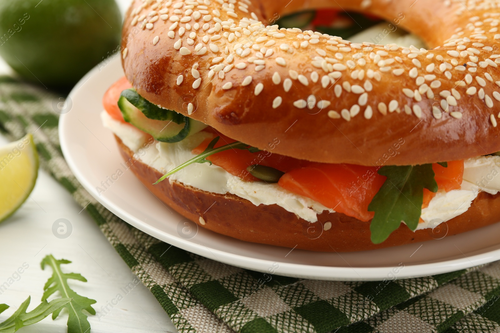 Photo of Delicious bagel with salmon, arugula and cream cheese on white wooden table, closeup