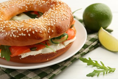 Photo of Delicious bagel with salmon, arugula and cream cheese on white wooden table, closeup