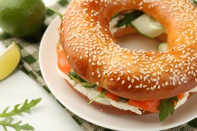 Photo of Delicious bagel with salmon, arugula and cream cheese on white table, closeup