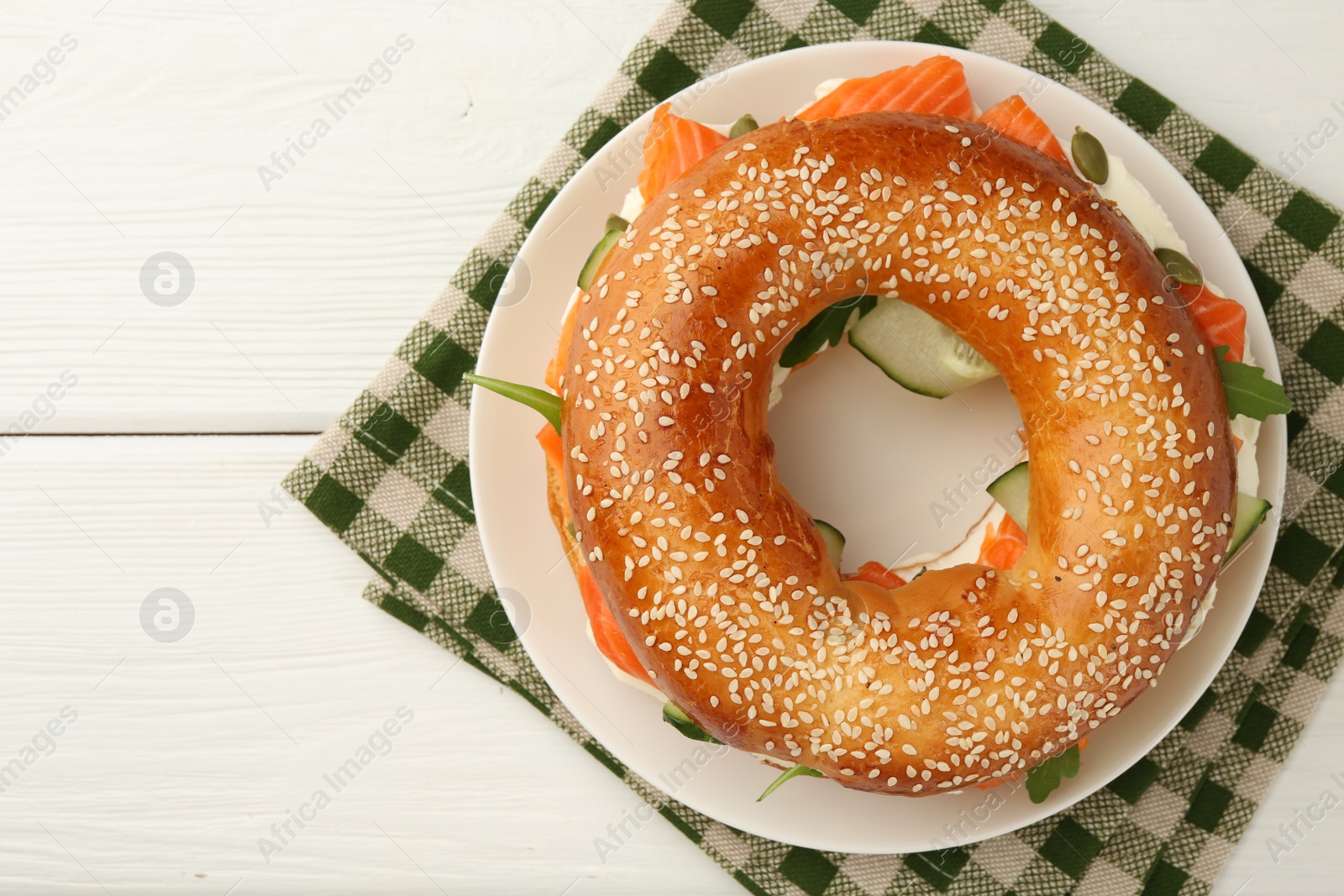 Photo of Delicious bagel with salmon, arugula and cream cheese on white wooden table, top view. Space for text