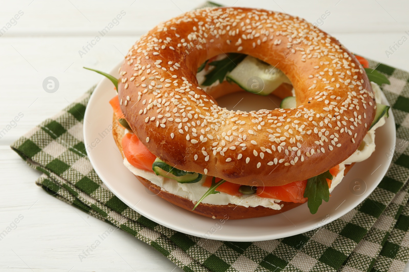 Photo of Delicious bagel with salmon, arugula and cream cheese on white wooden table, closeup