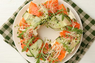 Photo of Half of delicious bagel with salmon, microgreens, arugula and cucumber on white wooden table, top view