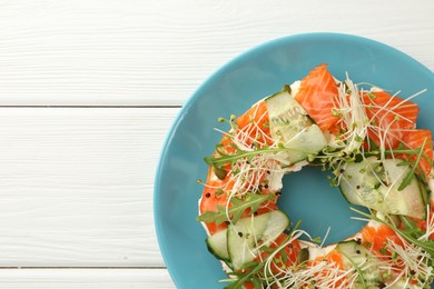 Photo of Half of delicious bagel with salmon, microgreens, arugula and cucumber on white wooden table, top view. Space for text