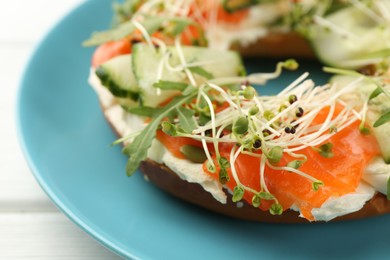 Photo of Half of delicious bagel with salmon, microgreens, arugula and cream cheese on white wooden table, closeup