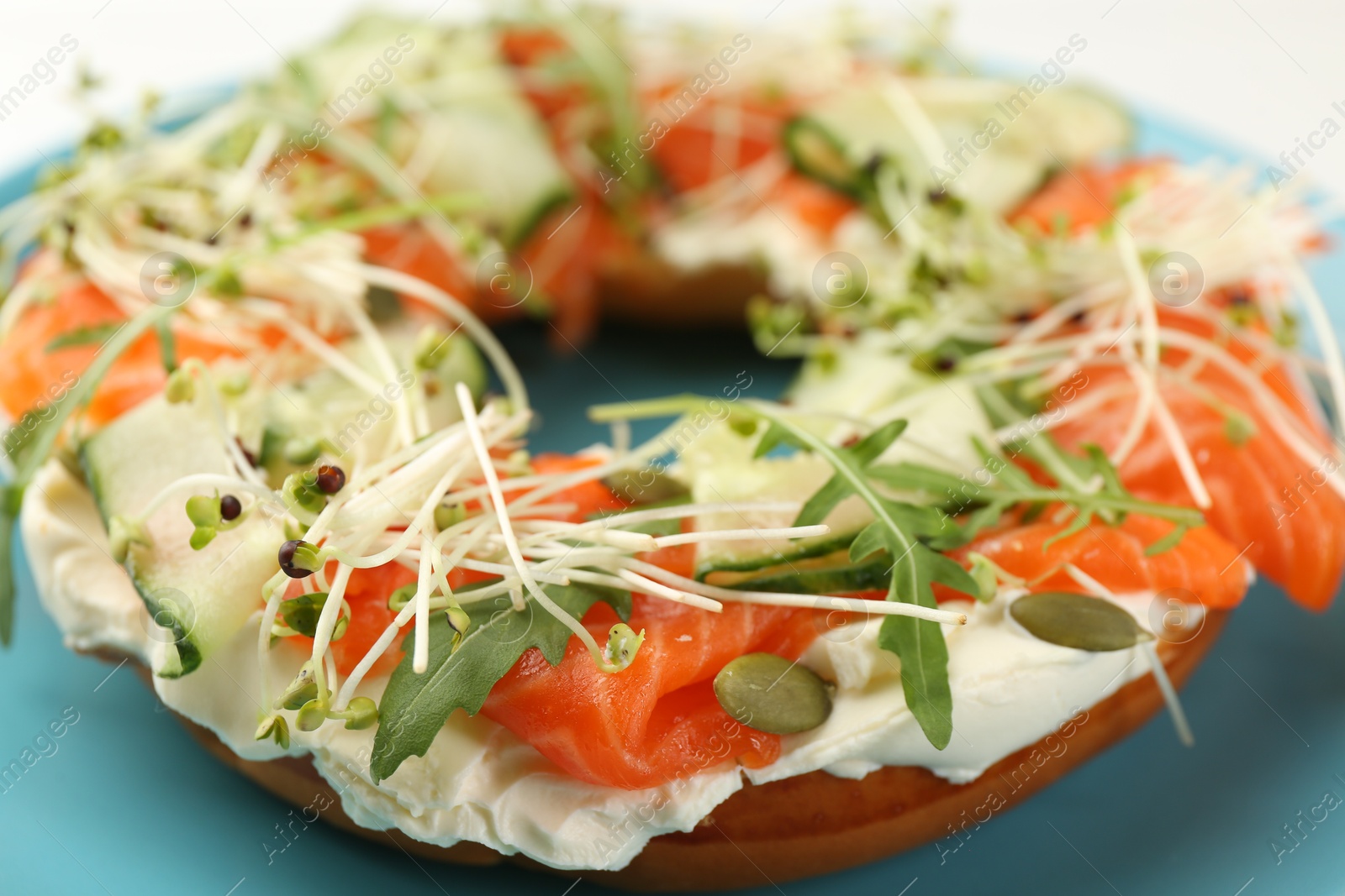 Photo of Half of delicious bagel with salmon, microgreens, arugula and cream cheese on plate, closeup