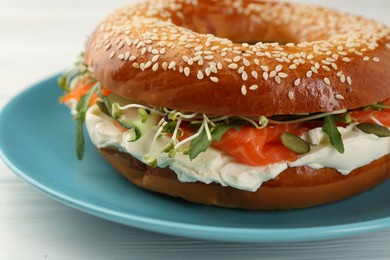 Photo of Delicious bagel with salmon, microgreens, arugula and cream cheese on white wooden table, closeup