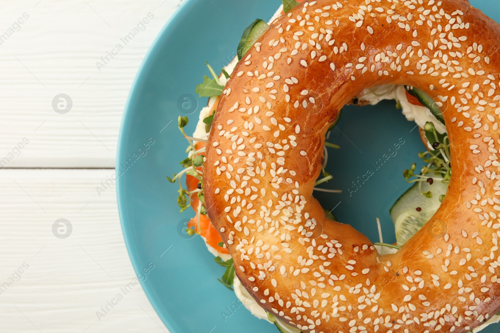 Photo of Delicious bagel with salmon, microgreens and cucumber on white wooden table, top view