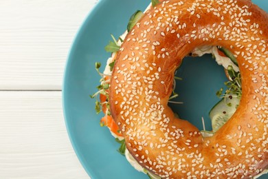 Photo of Delicious bagel with salmon, microgreens and cucumber on white wooden table, top view