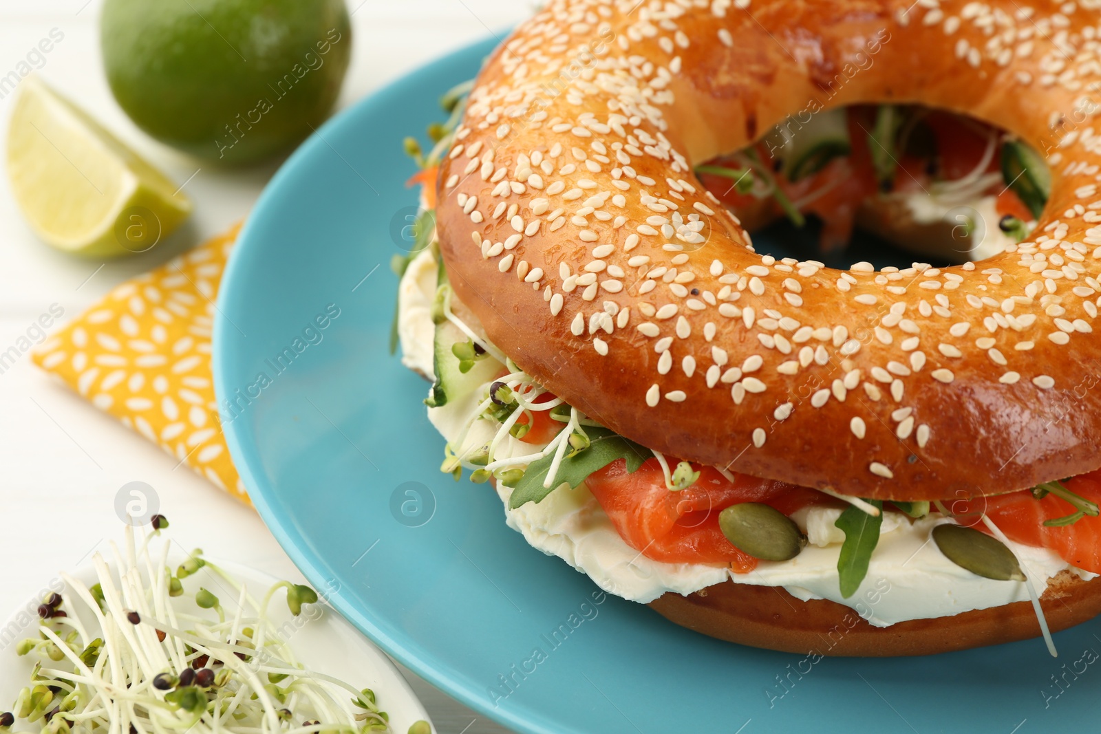 Photo of Delicious bagel with salmon, microgreens, arugula and cream cheese on white table, closeup