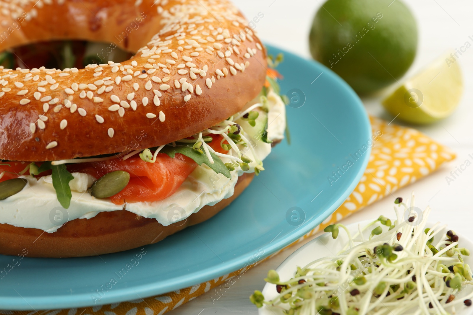 Photo of Delicious bagel with salmon, microgreens, arugula and cream cheese on white table, closeup