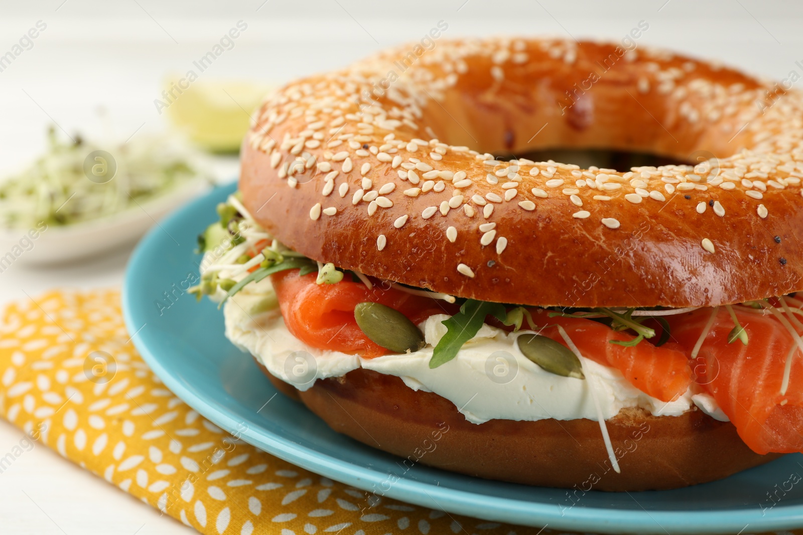 Photo of Delicious bagel with salmon, microgreens, arugula and cream cheese on white table, closeup