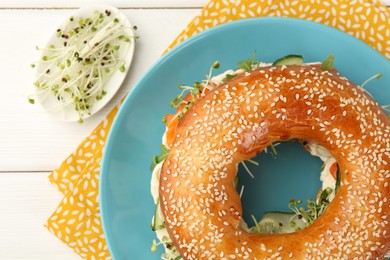 Photo of Delicious bagel with salmon, cucumber and microgreens on white wooden table, flat lay