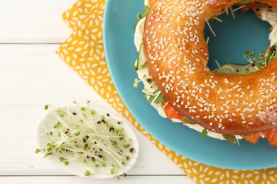 Photo of Delicious bagel with salmon, cucumber and microgreens on white wooden table, flat lay