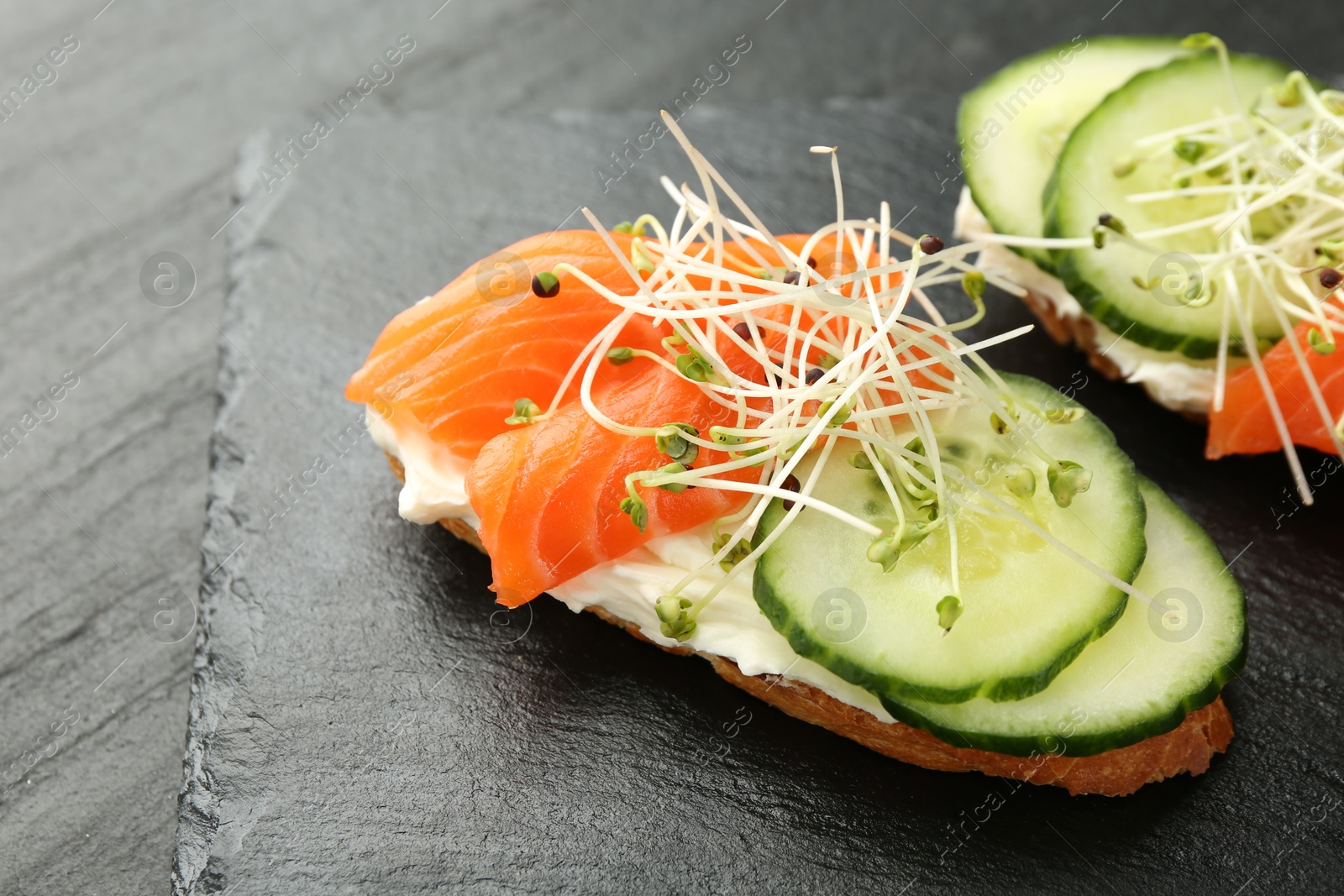 Photo of Delicious bruschette with salmon, cream cheese and cucumber on grey table, closeup