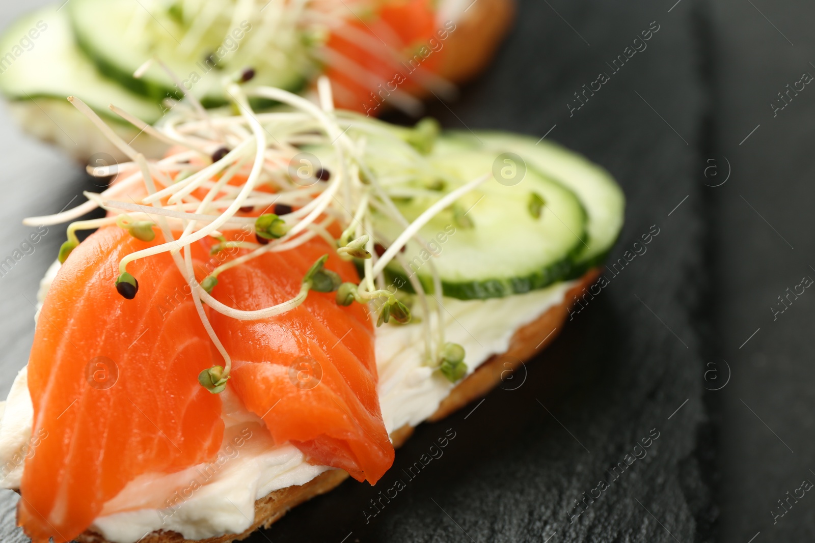 Photo of Delicious bruschette with salmon, cream cheese and cucumber on grey table, closeup