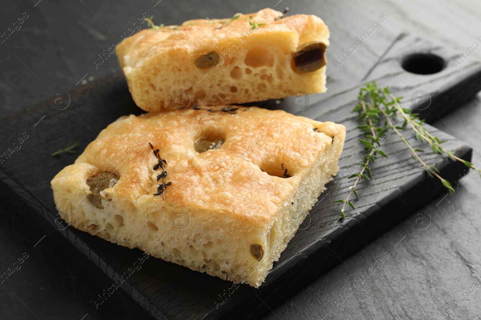 Photo of Pieces of delicious focaccia bread with olives and thyme on black table, closeup