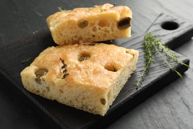 Photo of Pieces of delicious focaccia bread with olives and thyme on black table, closeup