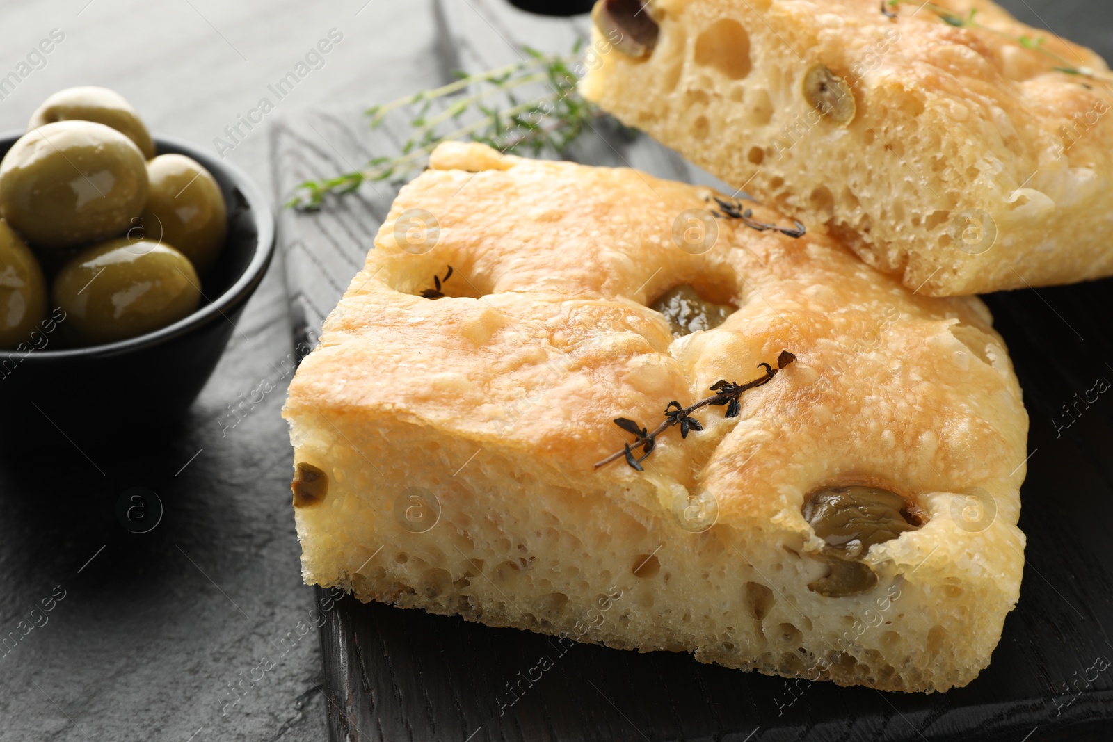 Photo of Pieces of delicious focaccia bread with olives and thyme on black table, closeup