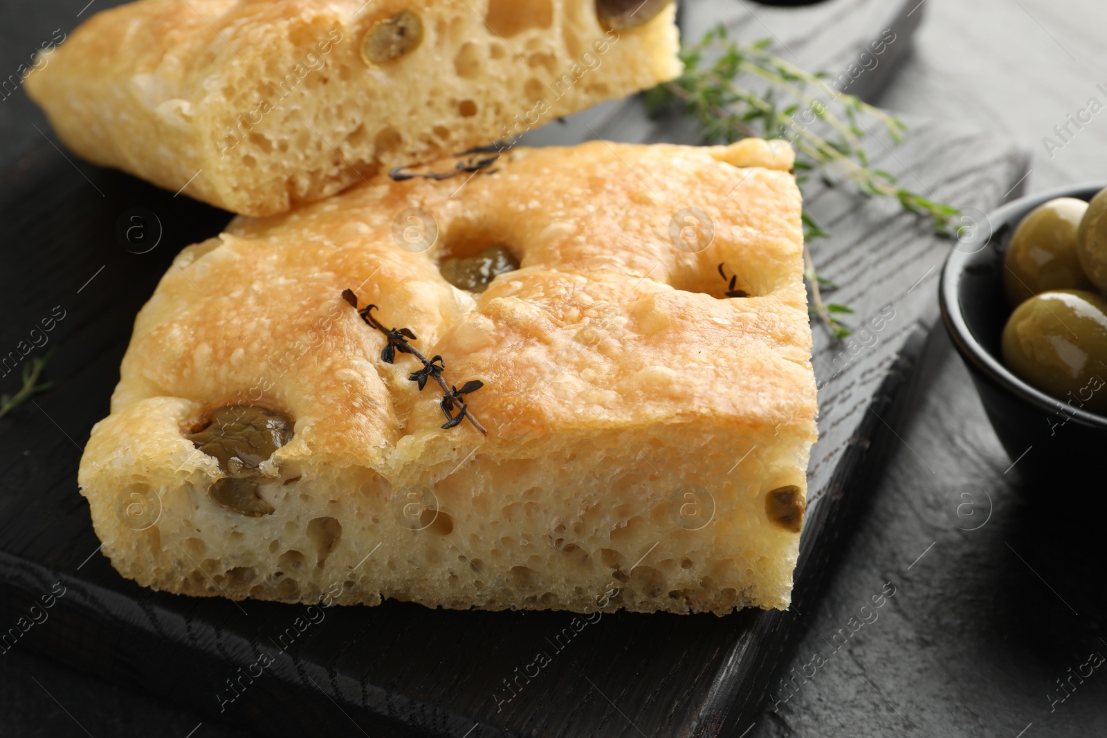 Photo of Pieces of delicious focaccia bread with olives and thyme on black table, closeup