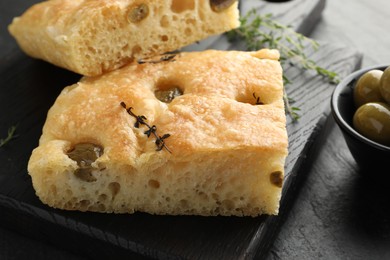 Photo of Pieces of delicious focaccia bread with olives and thyme on black table, closeup