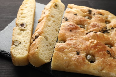 Photo of Pieces of delicious focaccia bread with olives and thyme on dark wooden table, closeup