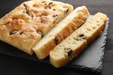 Photo of Pieces of delicious focaccia bread with olives and thyme on dark wooden table, closeup