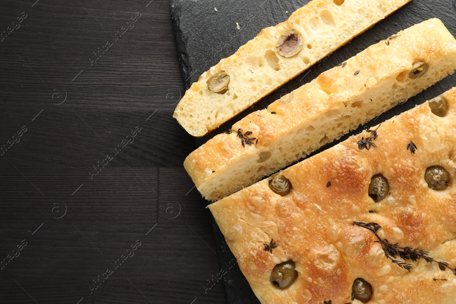 Photo of Pieces of delicious focaccia bread with olives and thyme on dark wooden table, top view. Space for text