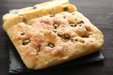 Photo of Pieces of delicious focaccia bread with olives and thyme on dark wooden table, closeup