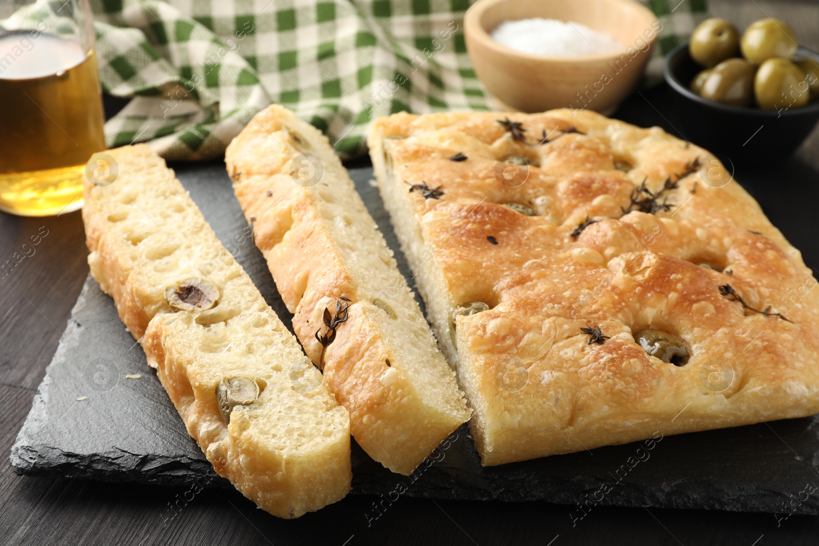 Photo of Pieces of delicious focaccia bread with olives and thyme on dark wooden table, closeup