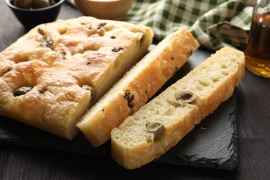 Photo of Pieces of delicious focaccia bread with olives and thyme on dark wooden table, closeup