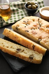 Photo of Pieces of delicious focaccia bread with olives and thyme on dark wooden table, closeup