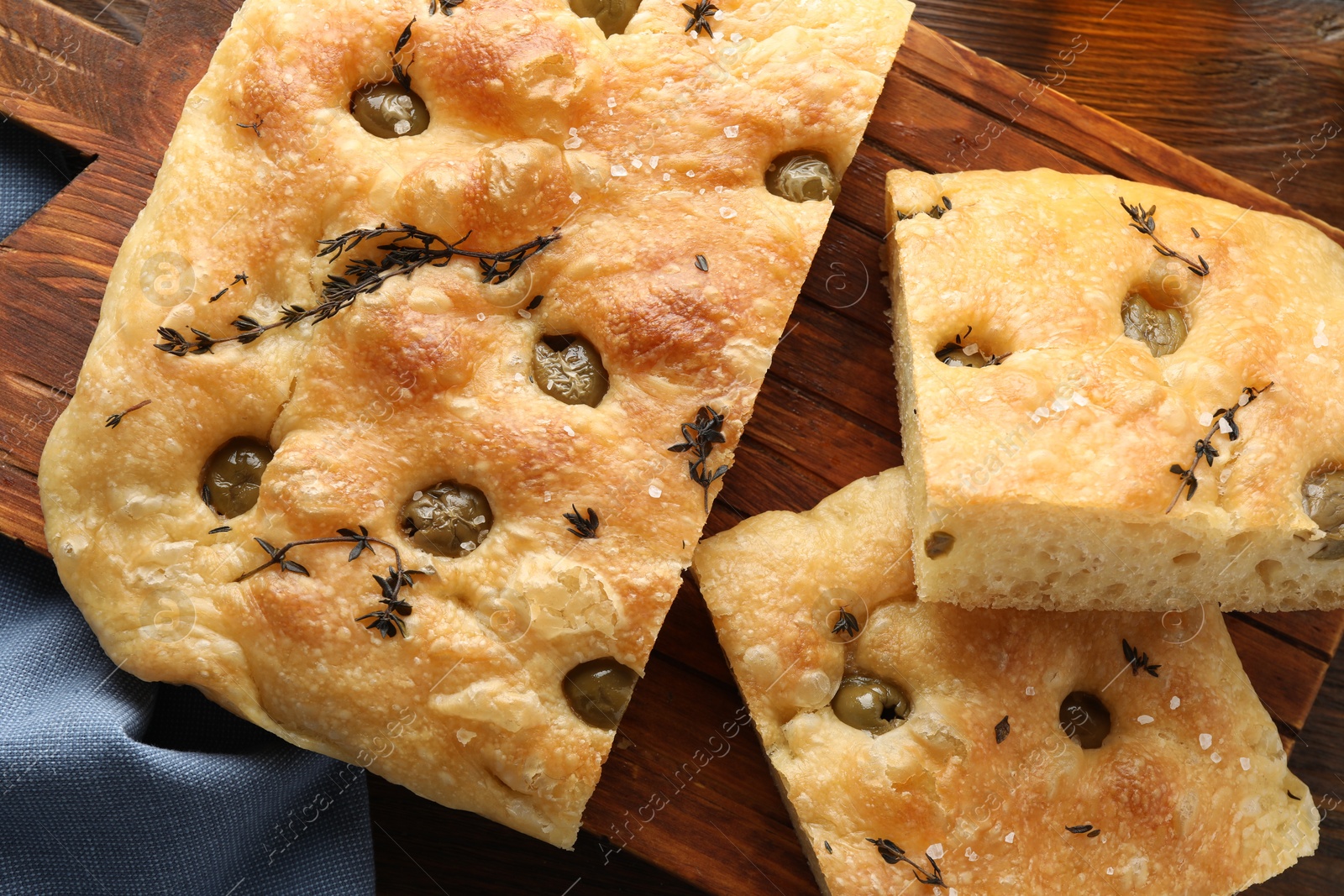 Photo of Pieces of delicious focaccia bread with olives and thyme on wooden table, top view